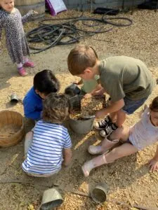 Children gathered around a metal bucket filled with soil and plants in a farm setting