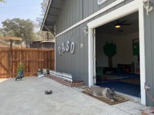 Gray building with white trim and large open garage door revealing colorful interior play space, white picket fence detail at entrance