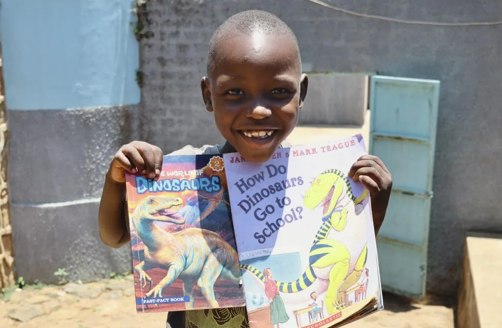 Child smiling while holding open two children's books about dinosaurs outdoors
